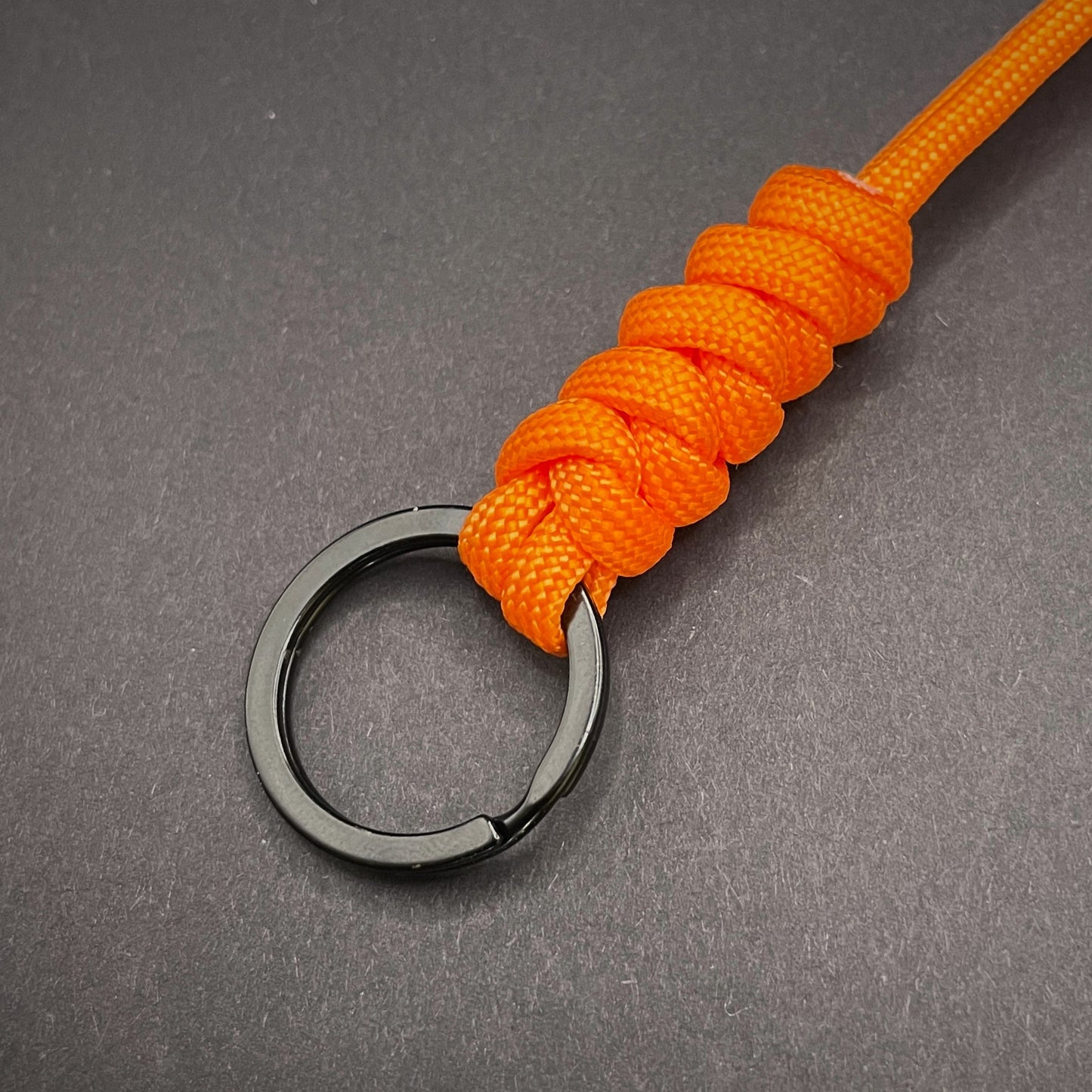 Orange 550 Paracord snake knot lanyard with black split ring, displayed on a dark textured background.