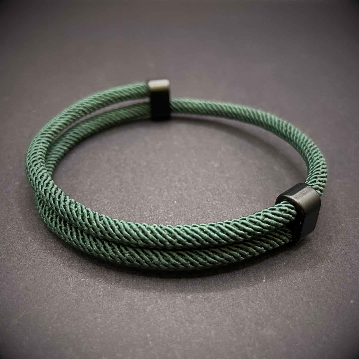Forrest Green Milan rope bracelet with black sliding clasps, displayed on a dark grey surface.