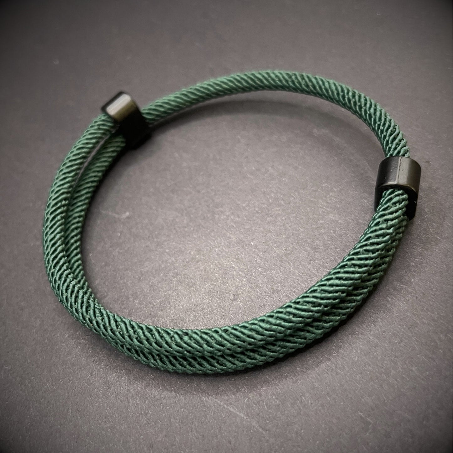 Forrest Green Milan rope bracelet with black sliding clasps, displayed on a dark grey surface.
