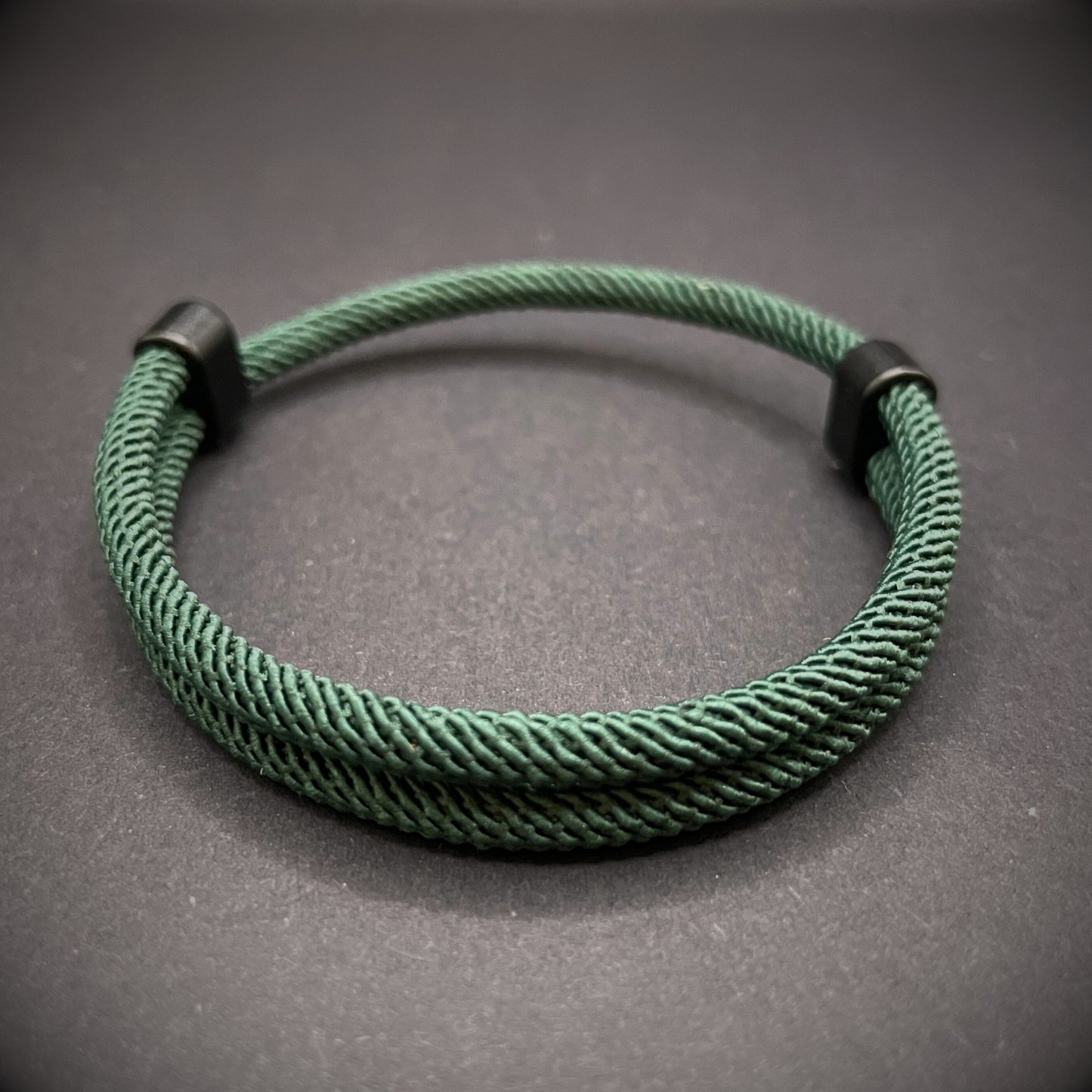 Forrest Green Milan rope bracelet with black sliding clasps, displayed on a dark grey surface.