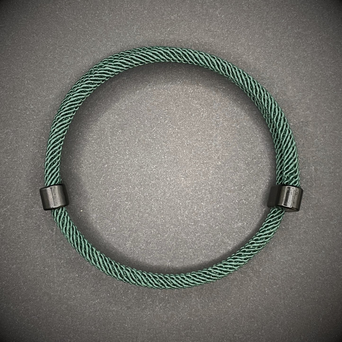 Forrest Green Milan rope bracelet with black sliding clasps, displayed on a dark grey surface.