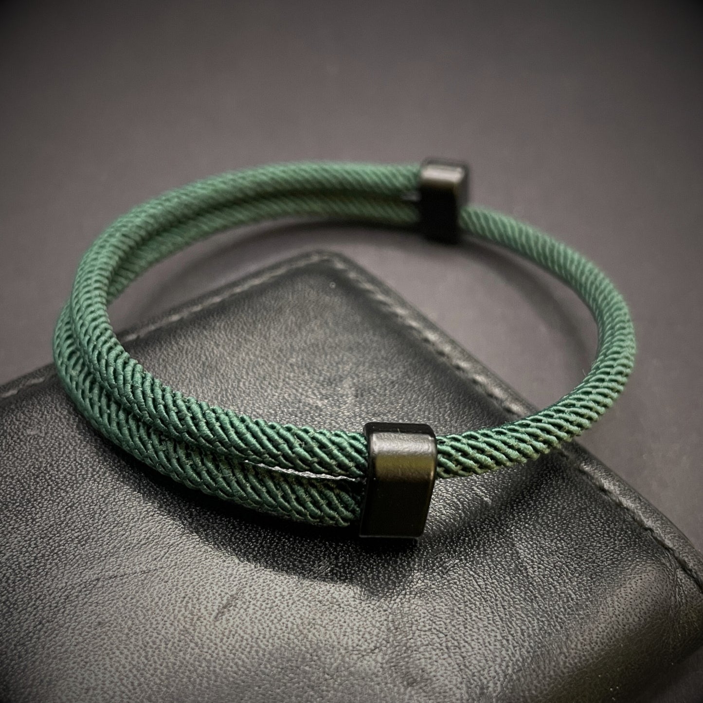 Forrest Green Milan rope bracelet with black sliding clasps, displayed on a dark grey surface.