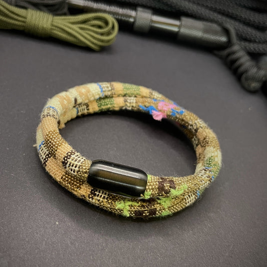 Khaki Boho rope bracelet with black magnetic clasps, displayed on a dark grey surface with EDC gear in the background.