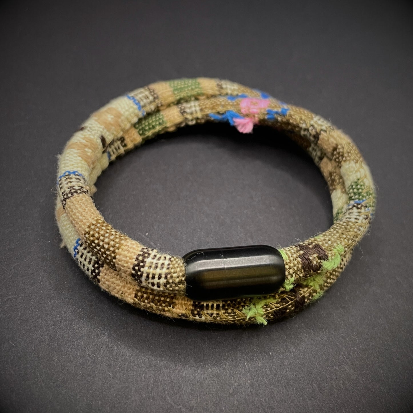 Khaki Boho rope bracelet with black magnetic clasps, displayed on a dark grey surface.