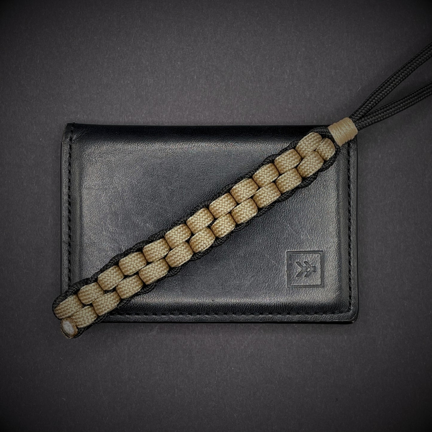 Flat lay of a Black and Khaki 550 Paracord knife lanyards on a dark grey background