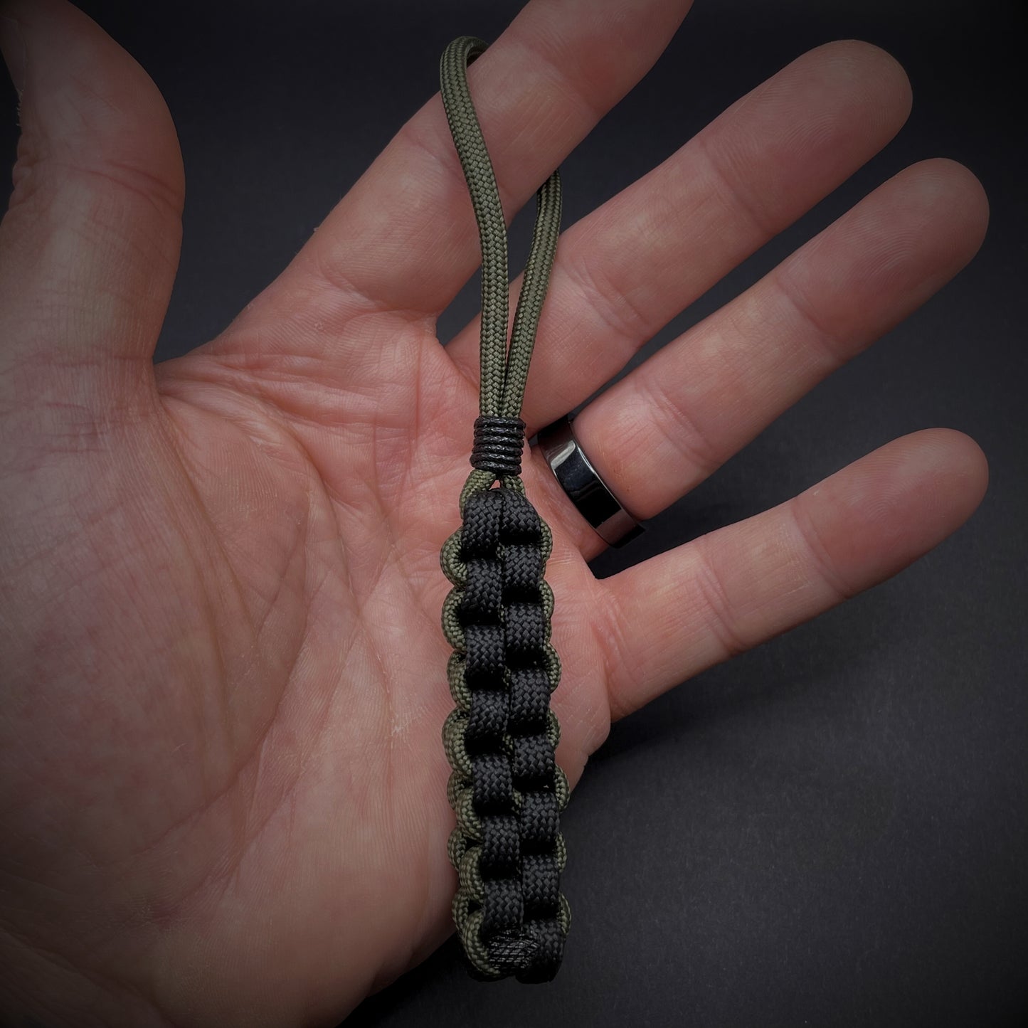 Flat lay of a 550 Paracord knife lanyard on a dark grey background in an open palmed hand