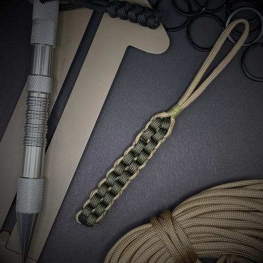 Flat lay of an Army Green and Khaki 550 Paracord knife lanyards on a dark grey background surrounded by EDC items