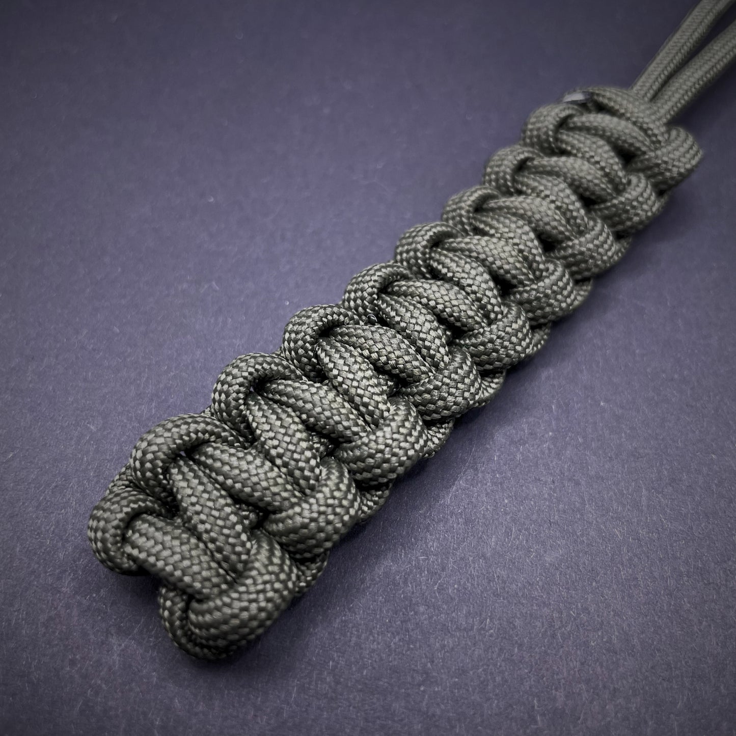 Flat lay of Army Green 550 Paracord knife lanyard on a dark grey background