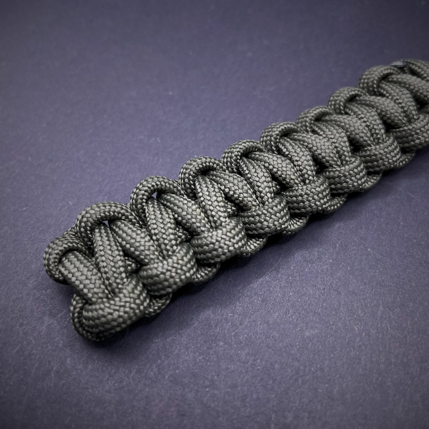 Flat lay of Army Green 550 Paracord knife lanyard on a dark grey background