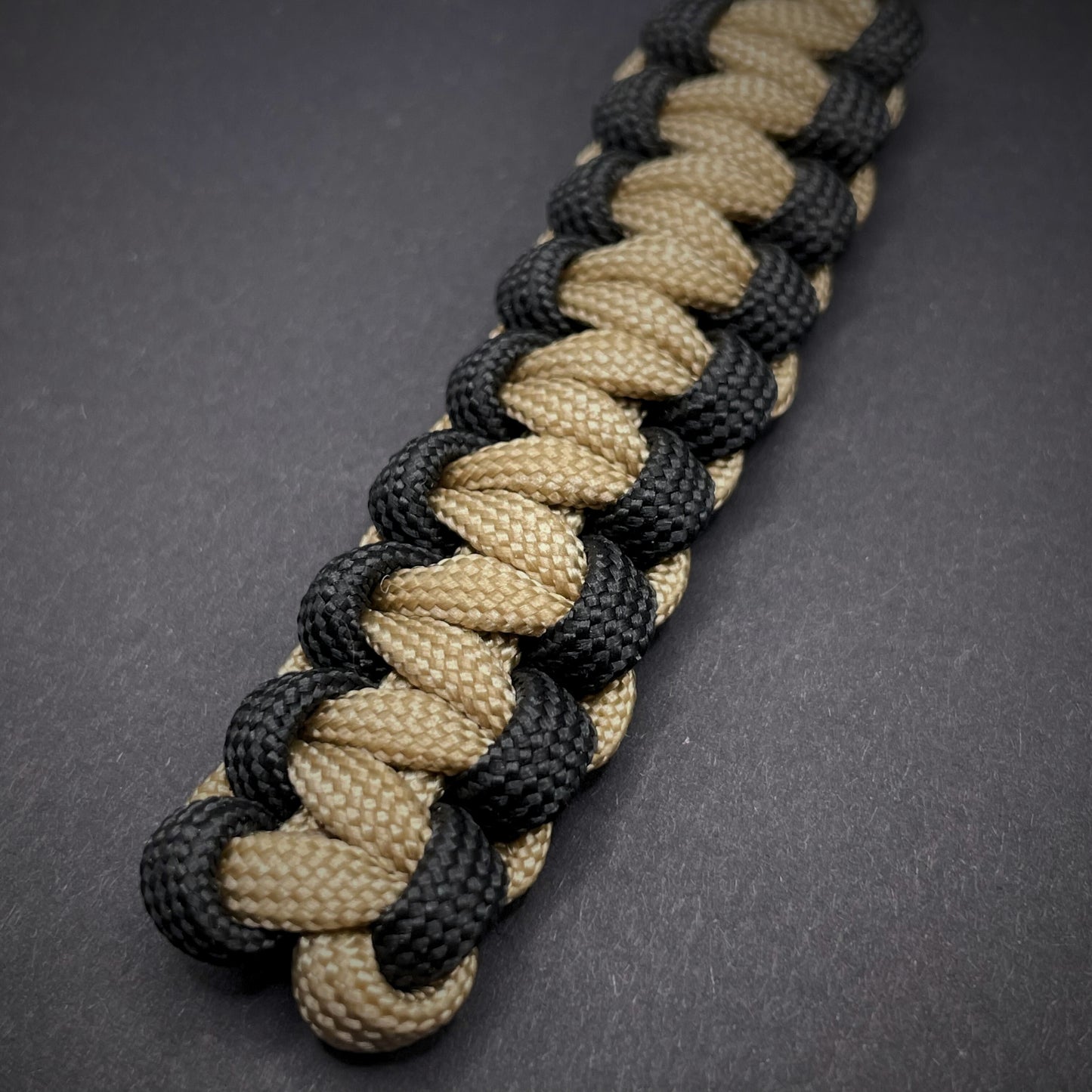 Flat lay of Khaki and Black 550 Paracord knife lanyard on a dark grey surface
