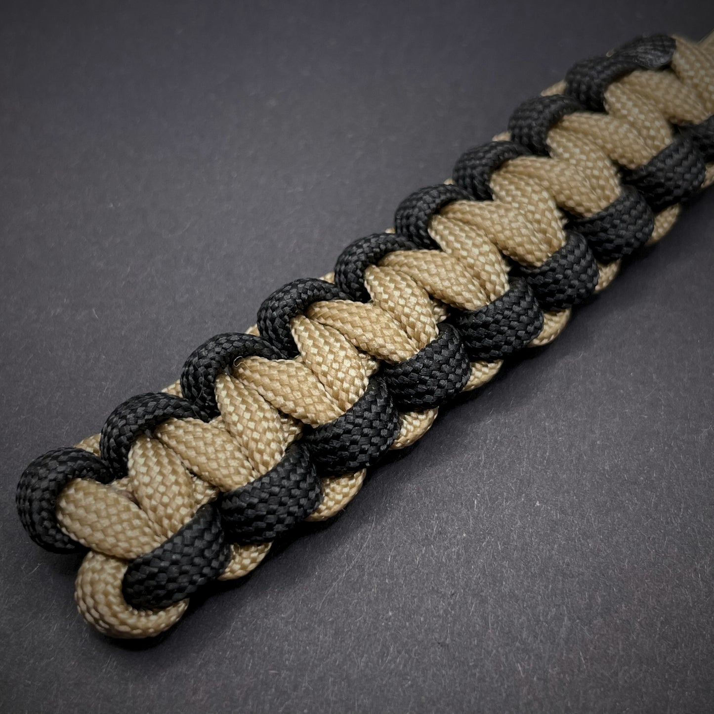Flat lay of Khaki and Black 550 Paracord knife lanyard on a dark grey surface