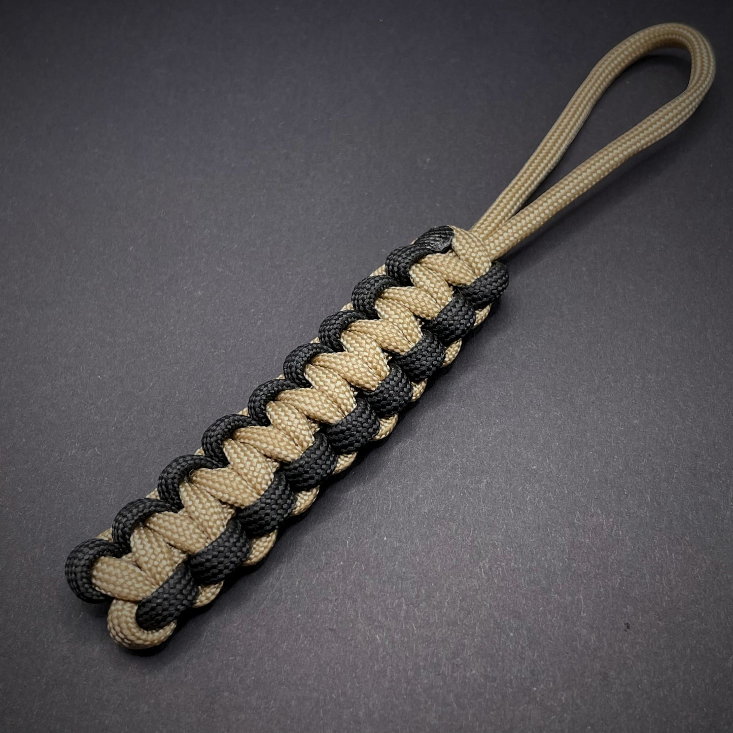 Flat lay of Khaki and Black 550 Paracord knife lanyard on a dark grey surface