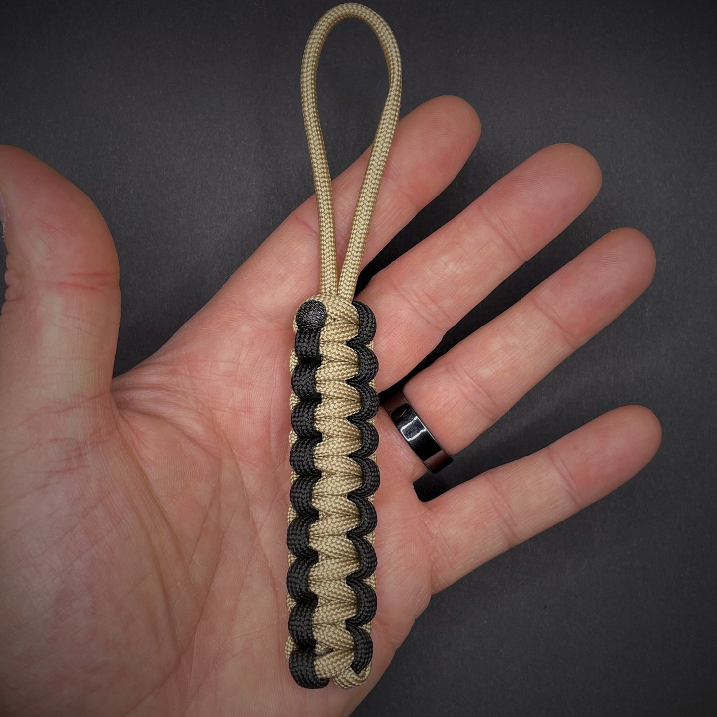 Flat lay of Khaki and Black 550 Paracord knife lanyard on a dark grey surface