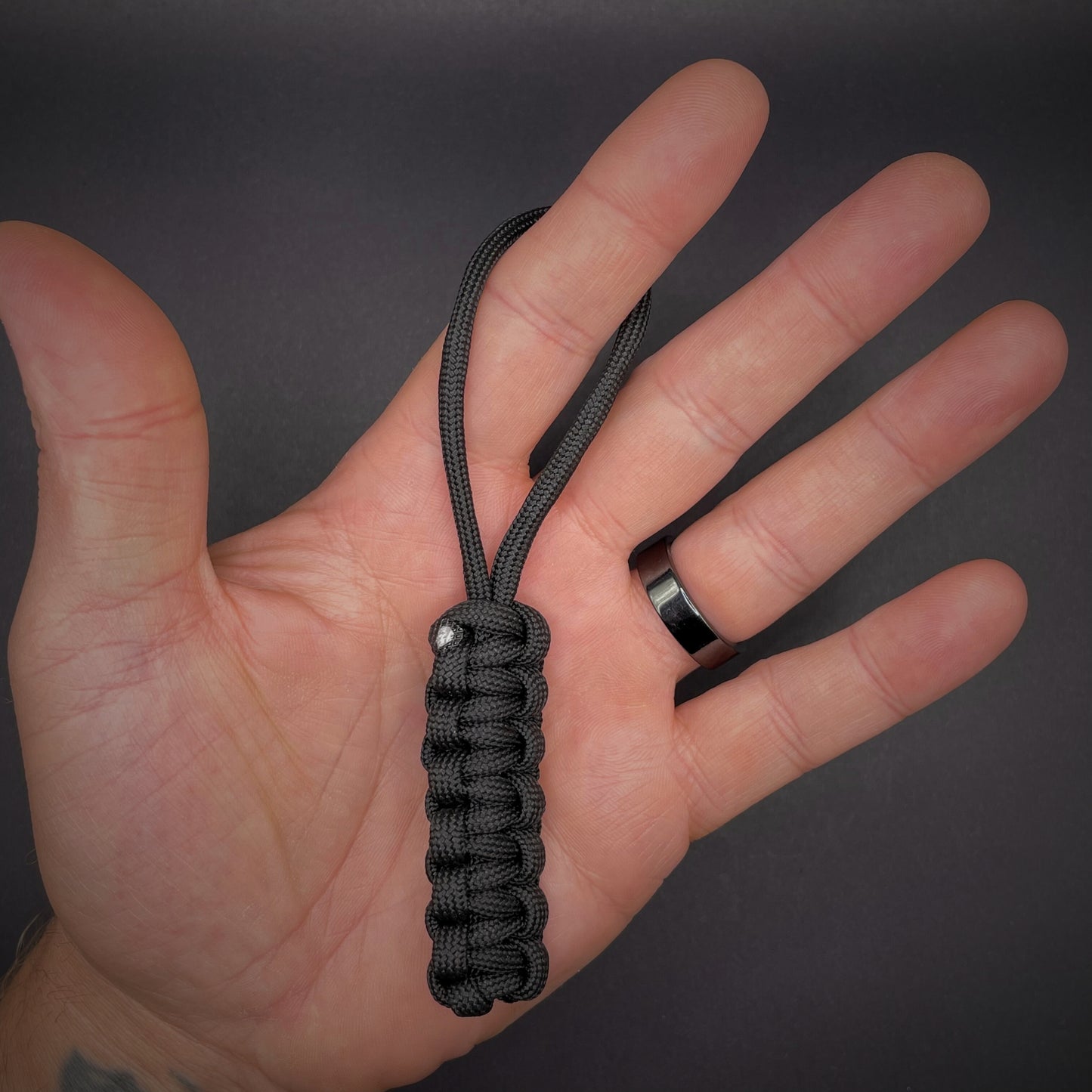 Flat lay of black 550 Paracord knife lanyard on a dark grey background