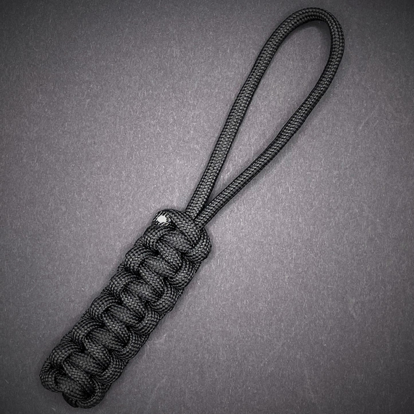 Flat lay of Black 550 Paracord knife lanyard on a dark grey background