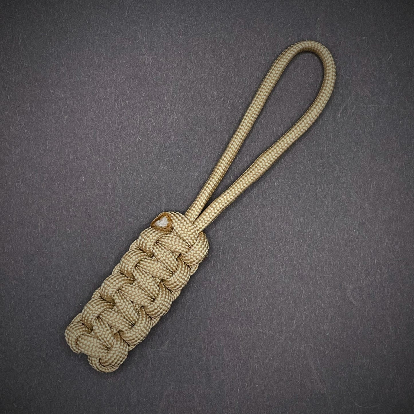Flat lay of Khaki 550 Paracord knife lanyard on a dark grey background