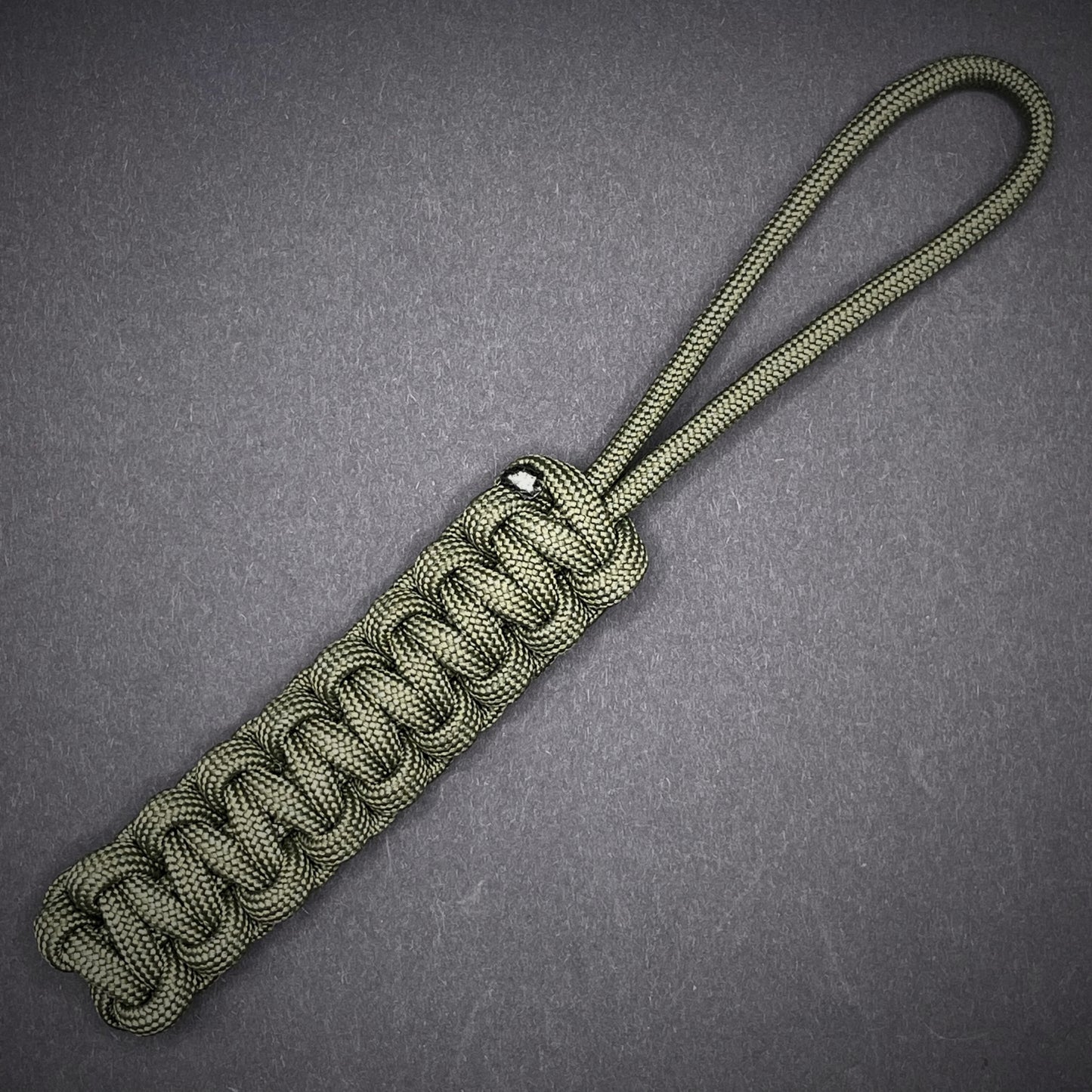 Flat lay of Army Green 550 Paracord knife lanyard on a dark grey background