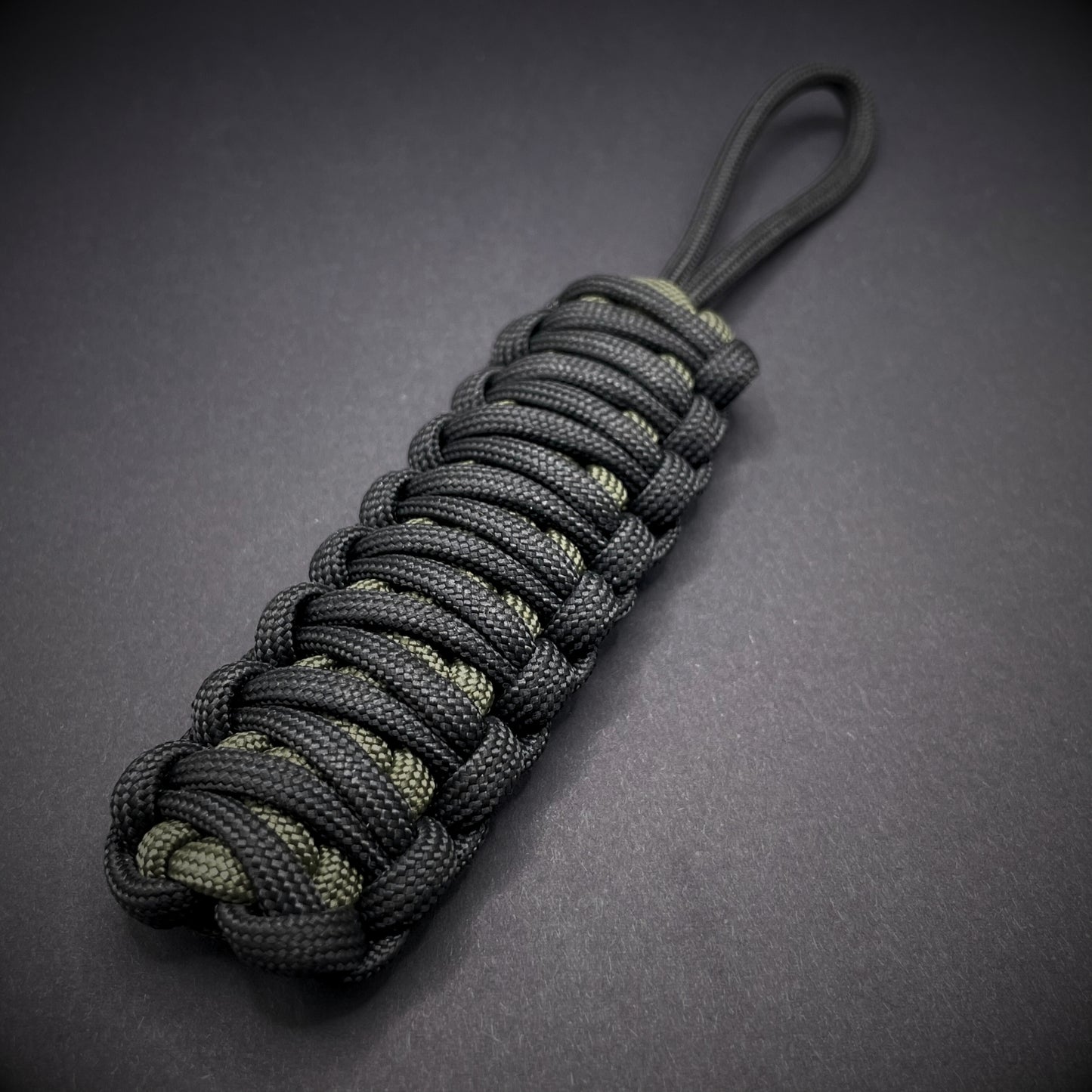 Flat lay of a black and army green 550 Paracord knife lanyards on a dark grey background