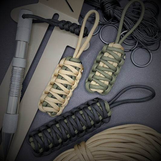 Flat lay of 3 550 Paracord knife lanyard on a dark grey background surrounded by EDC items