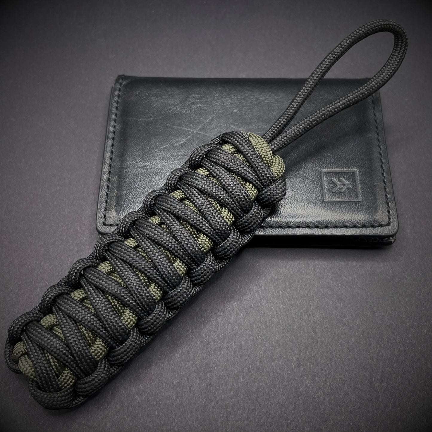 Flat lay of a black and army green 550 Paracord knife lanyards on a dark grey background