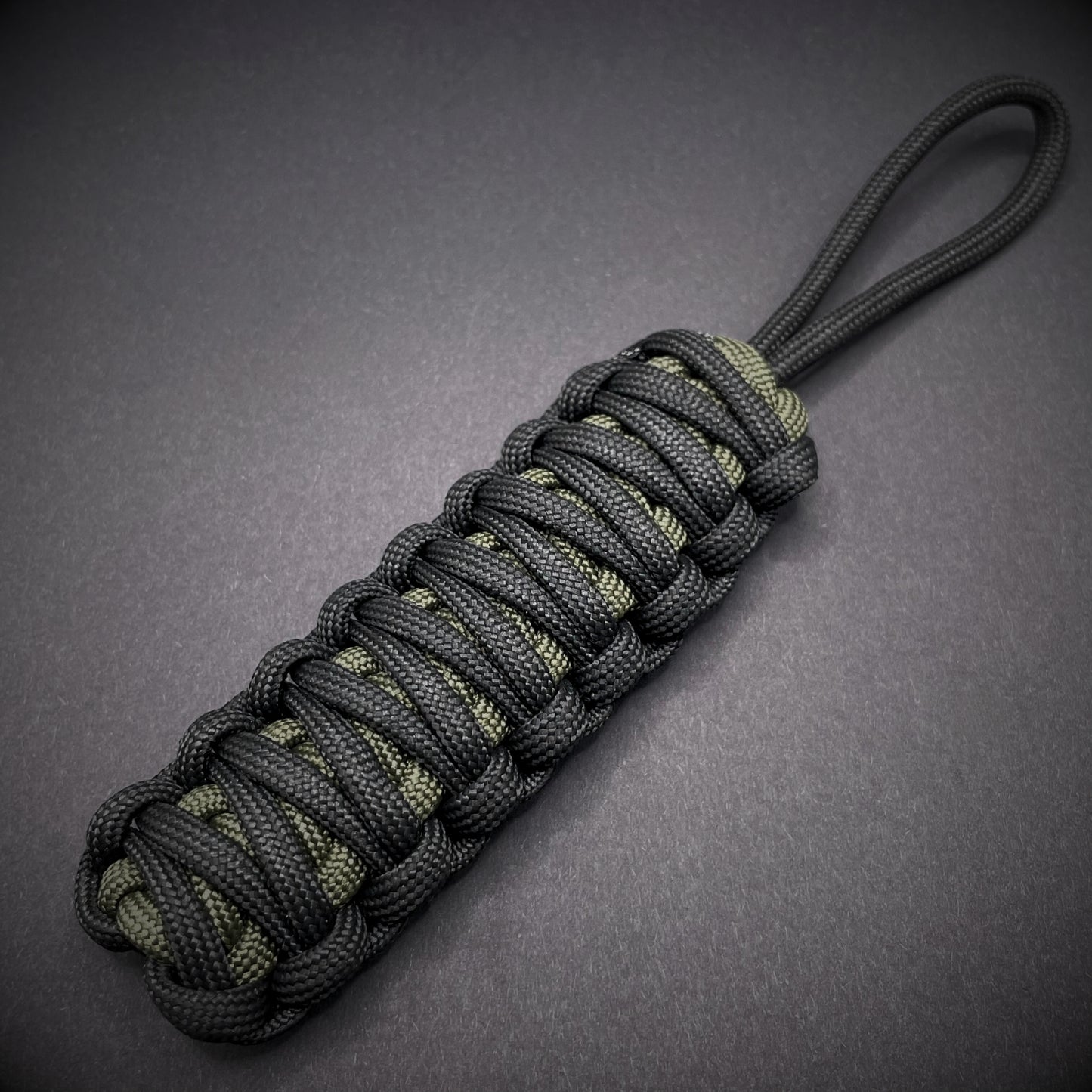 Flat lay of a black and army green 550 Paracord knife lanyards on a dark grey background