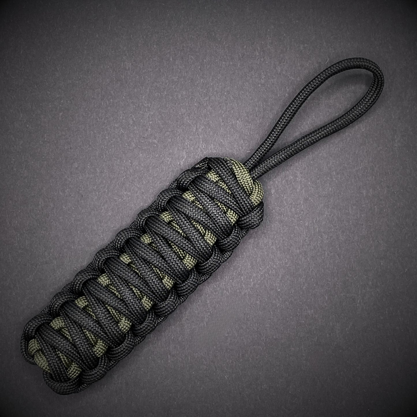 Flat lay of a black and army green 550 Paracord knife lanyards on a dark grey background