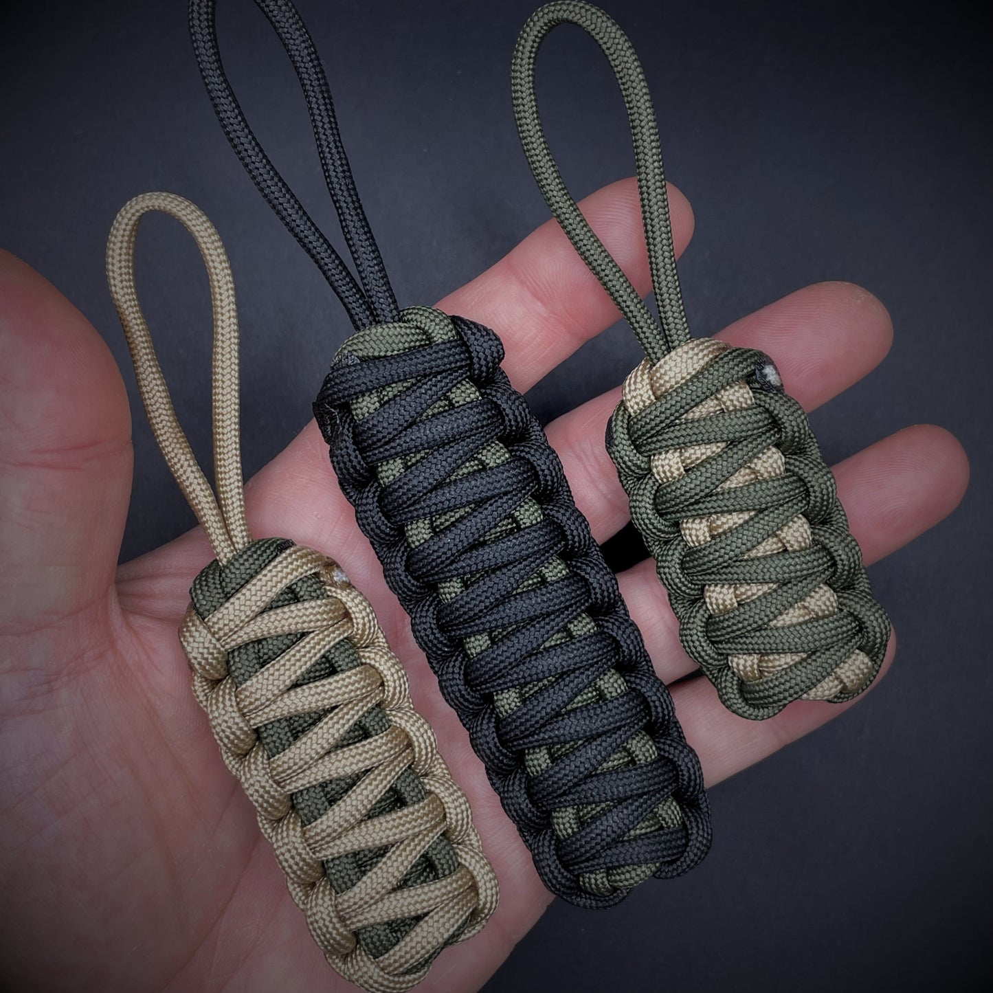 Flat lay of 3 550 Paracord knife lanyards in an open palmed hand over a dark grey background