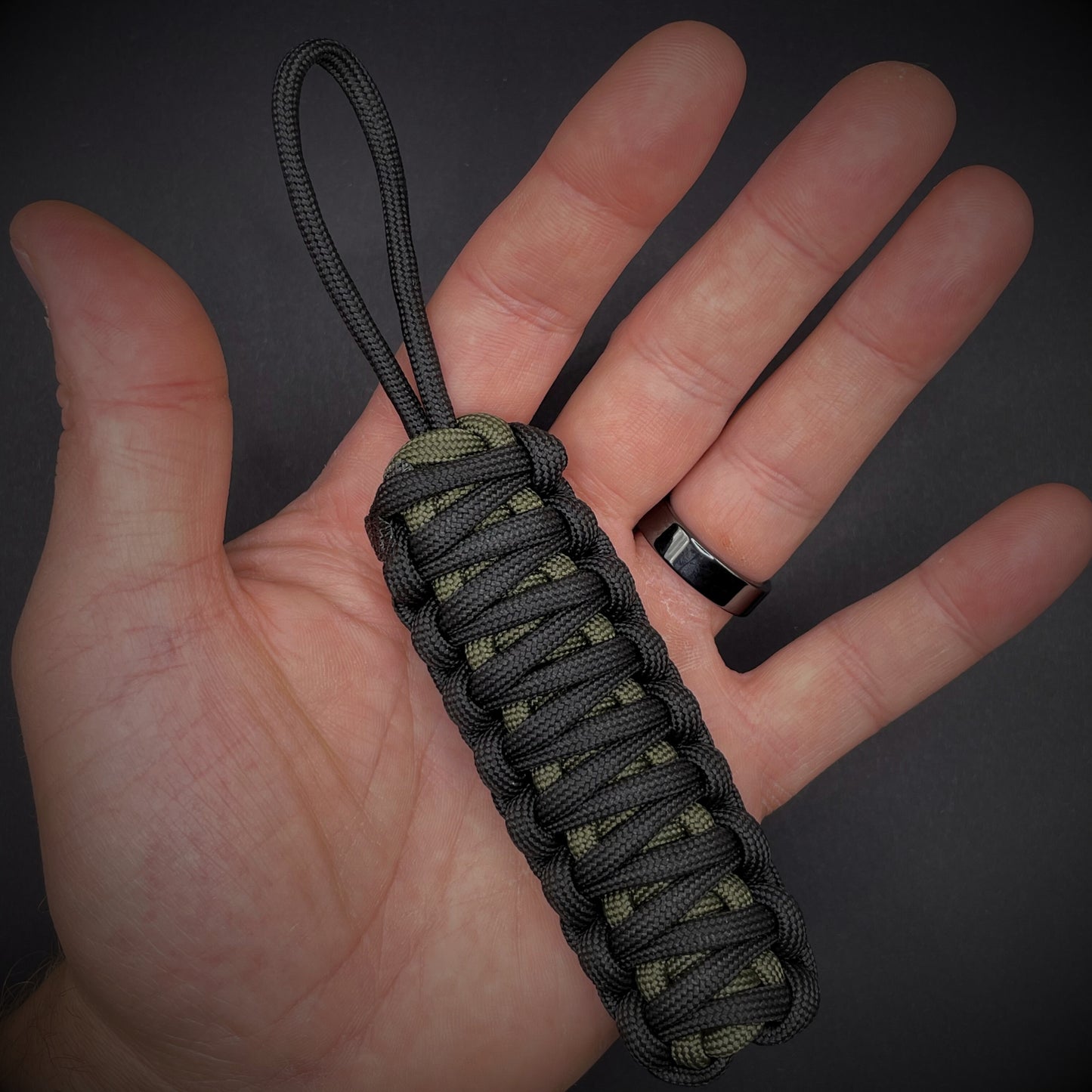 Flat lay of 3 550 Paracord knife lanyards in an open palmed hand over a dark grey background