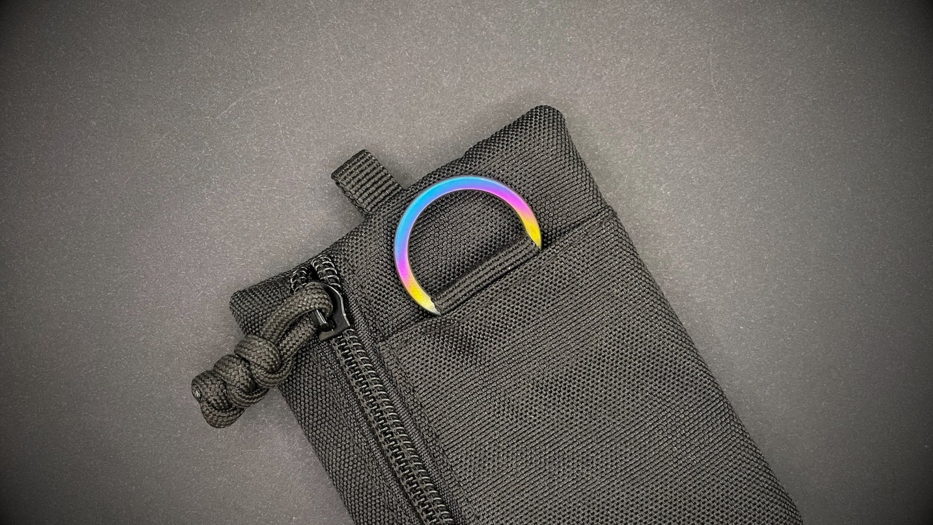 An Sunset Titanium Split Ring on a black pouch laid on a dark grey background