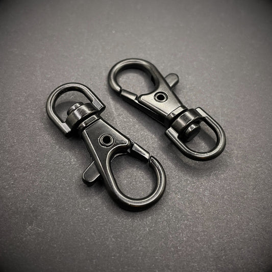 A close up image of 2 black keychain lobster clips arranged on a dark grey surface.