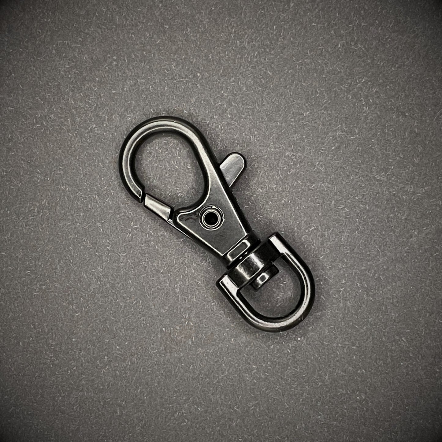 A close up image of a black keychain lobster clip arranged on a dark grey surface.