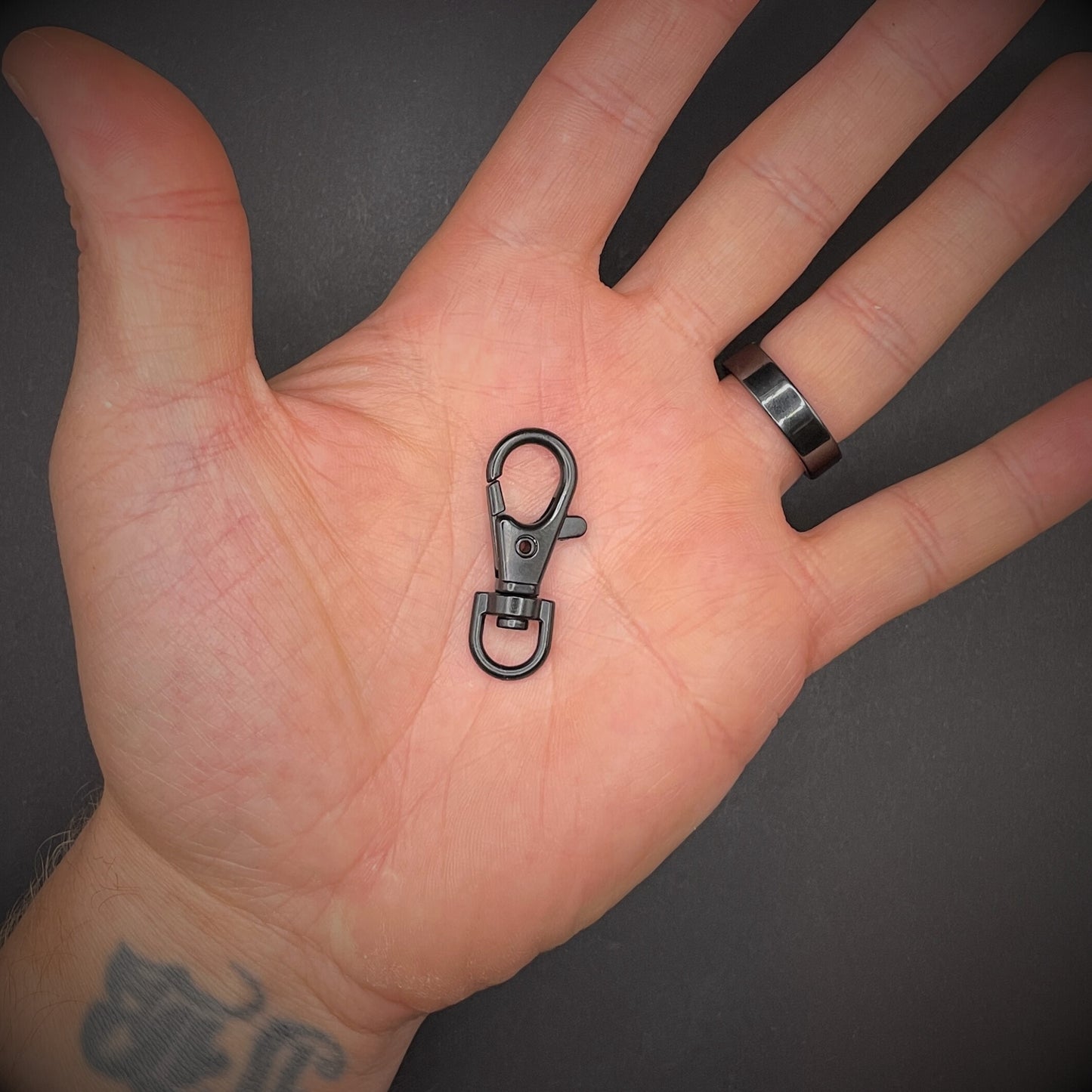 A close up image of a black keychain lobster clip arranged in a an open palm over a dark grey surface.