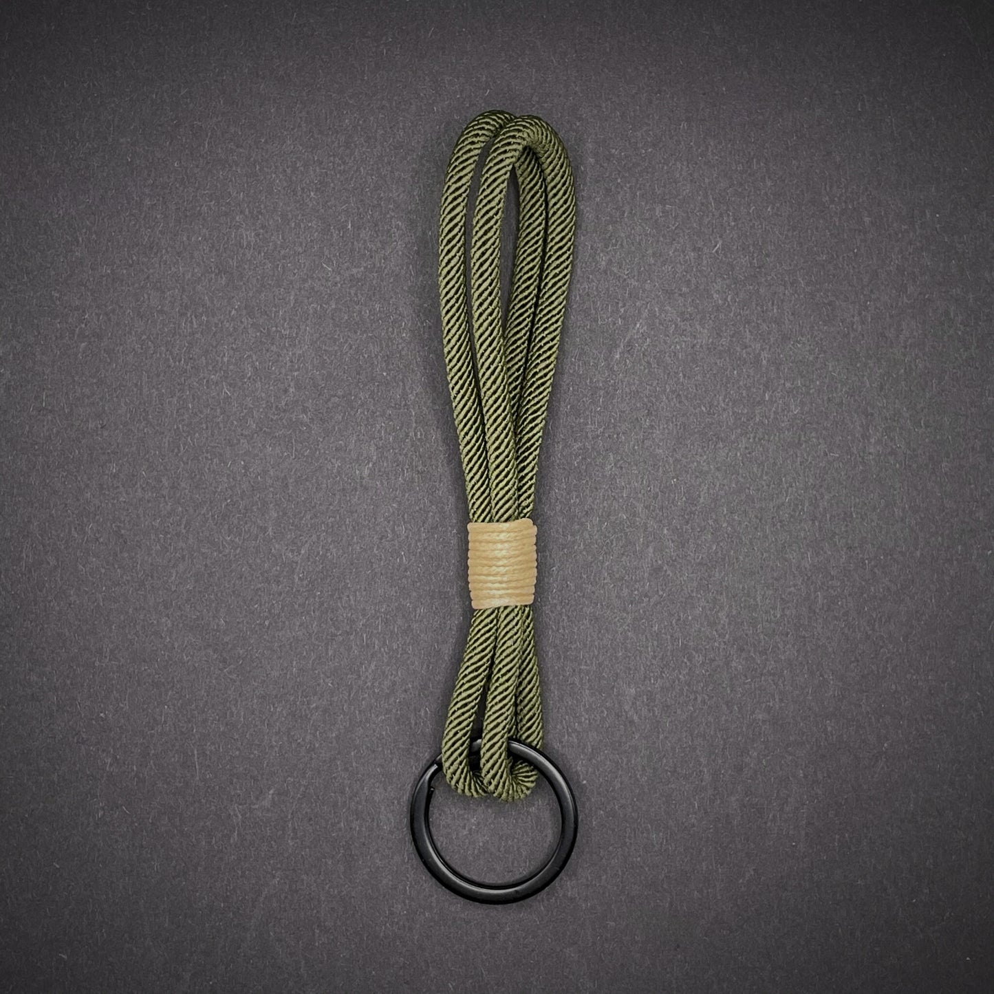 Flat lay of Green Milan Rope keychain with tan cotton whipping on a dark background.