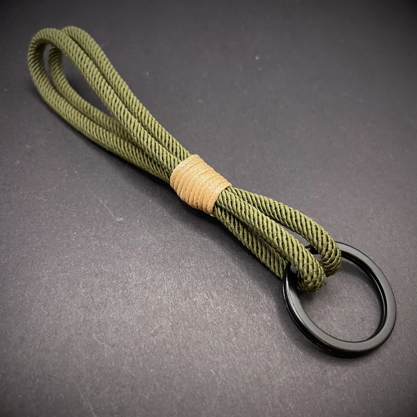Flat lay of Green Milan Rope keychain with tan cotton whipping on a dark background.