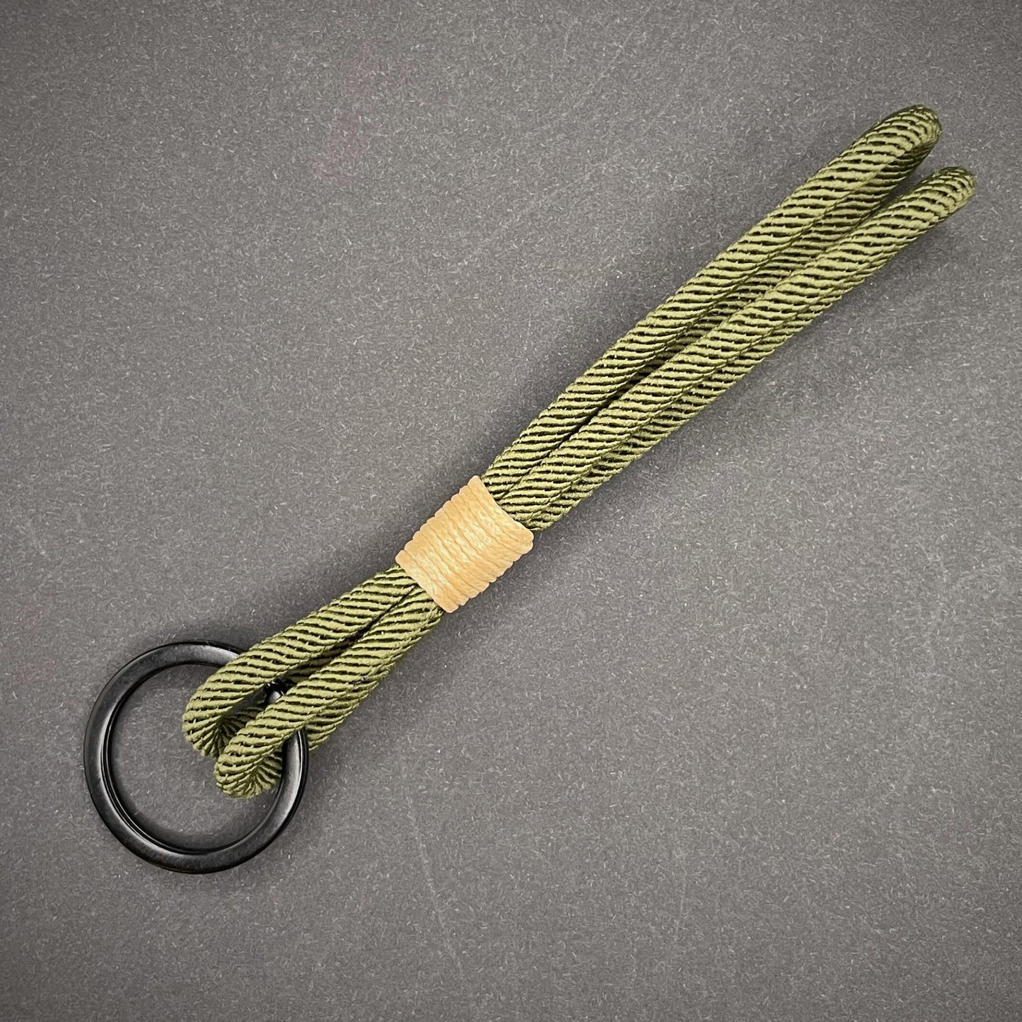 Flat lay of Green Milan Rope keychain with tan cotton whipping on a dark background.
