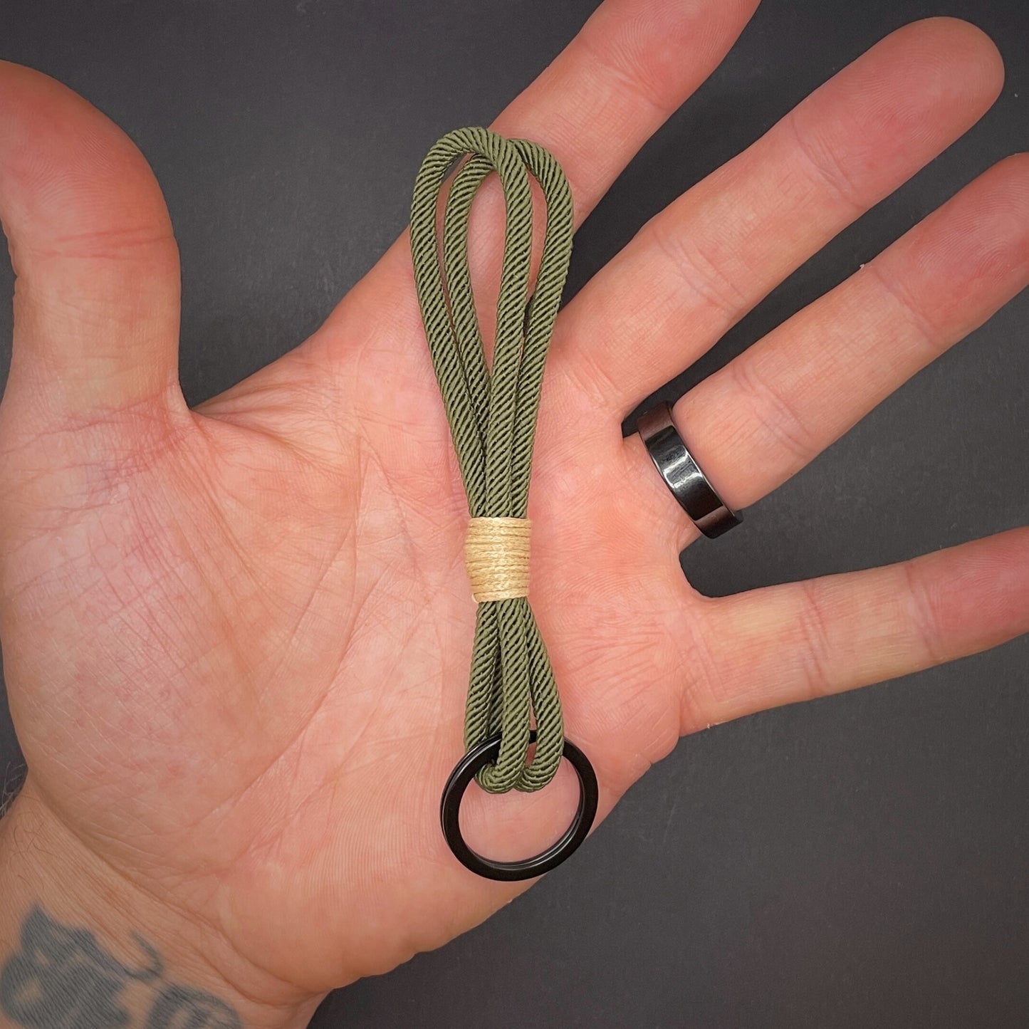 Flat lay of Green Milan Rope keychain with tan cotton whipping on a dark background.