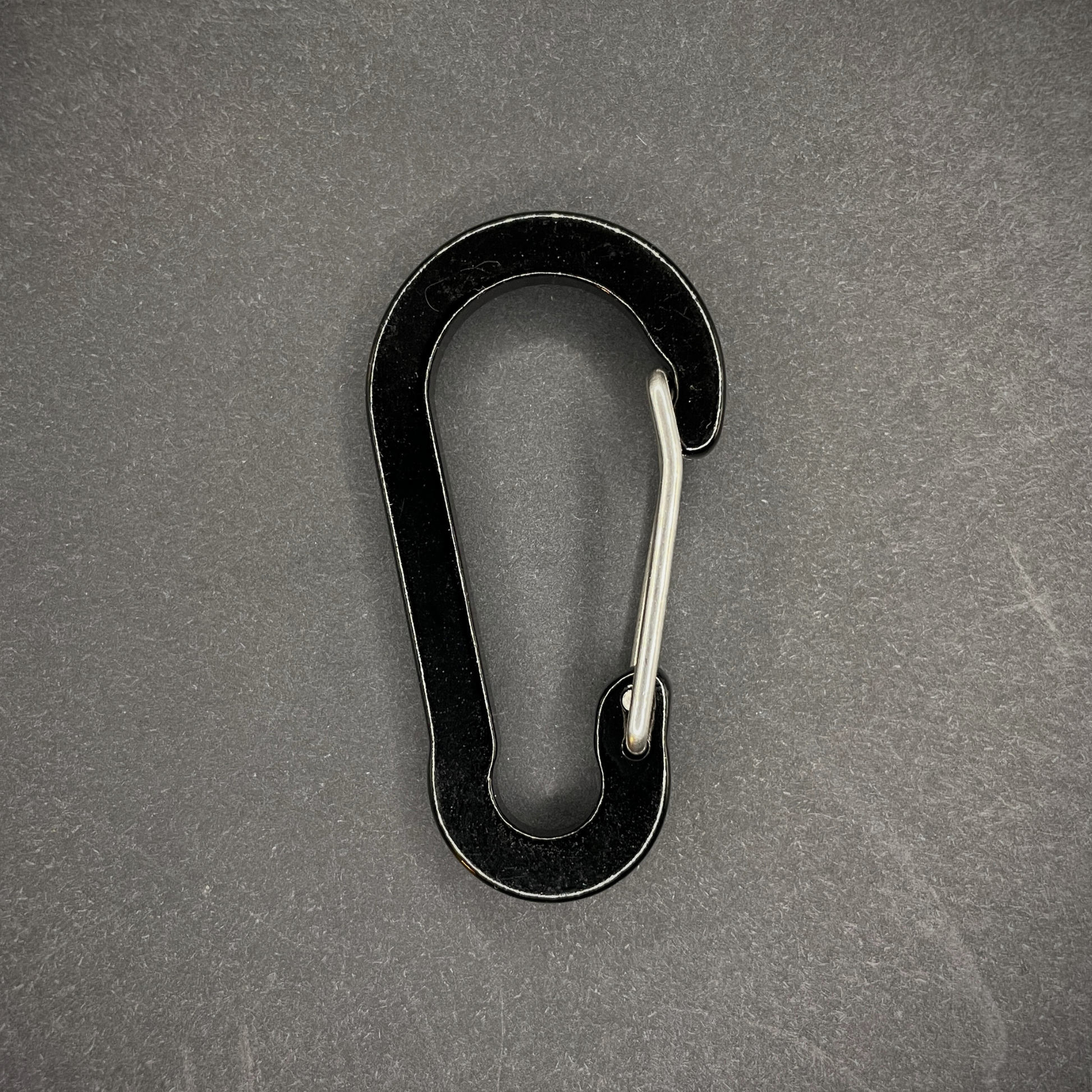 Black aluminium carabiner, arranged on a dark surface.