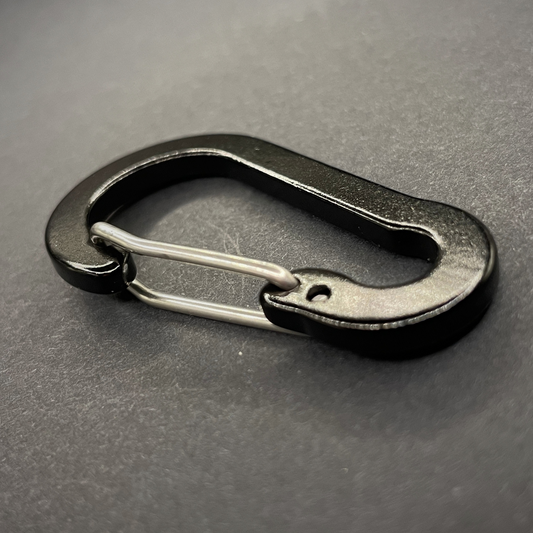 An angled view of a Black Anodised aluminium carabiner, arranged on a dark surface