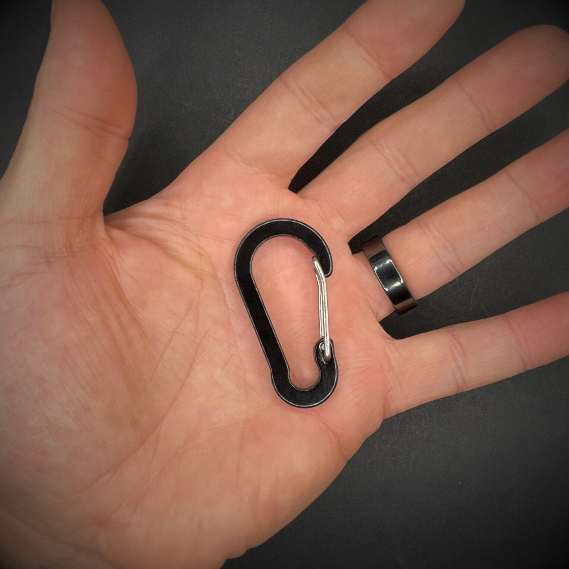 Black aluminium carabiner in the centre of a hand held above a dark surface.