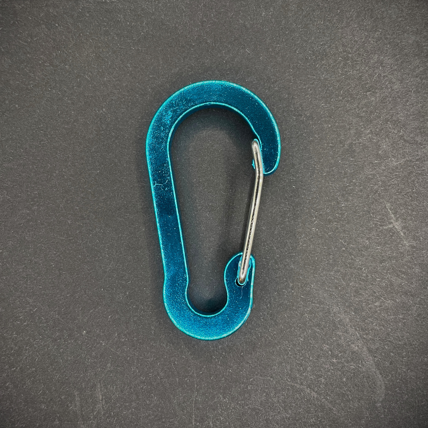 Blue Anodised aluminium carabiner, arranged on a dark surface.