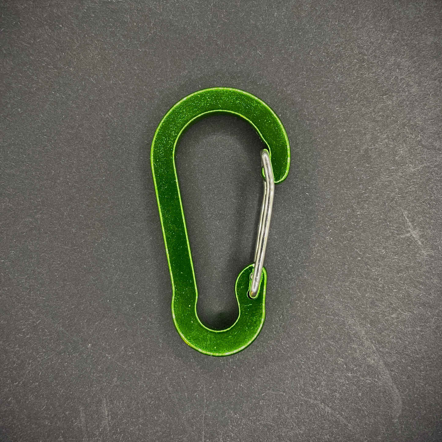 Green Anodised aluminium carabiner, arranged on a dark surface.