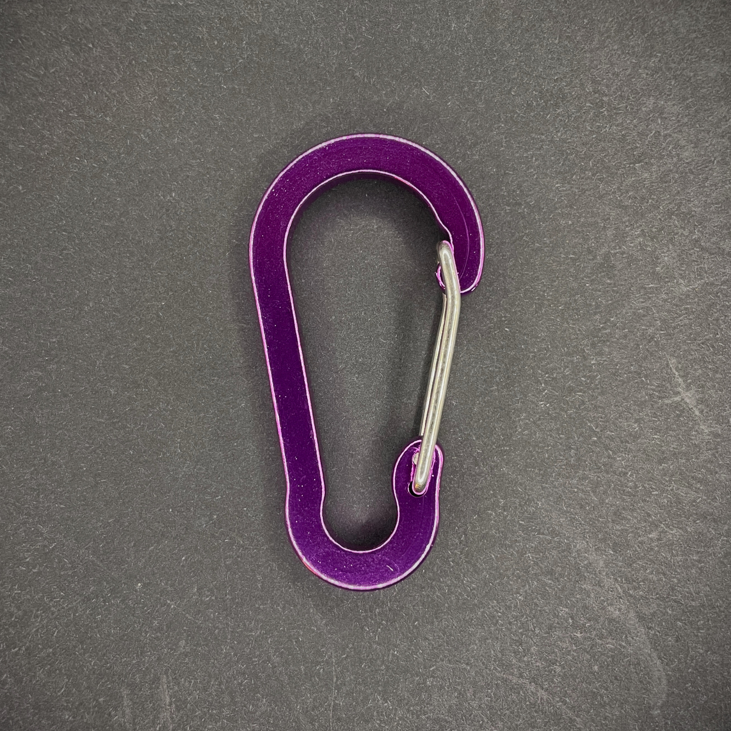 Purple Anodised aluminium carabiner, arranged on a dark surface.