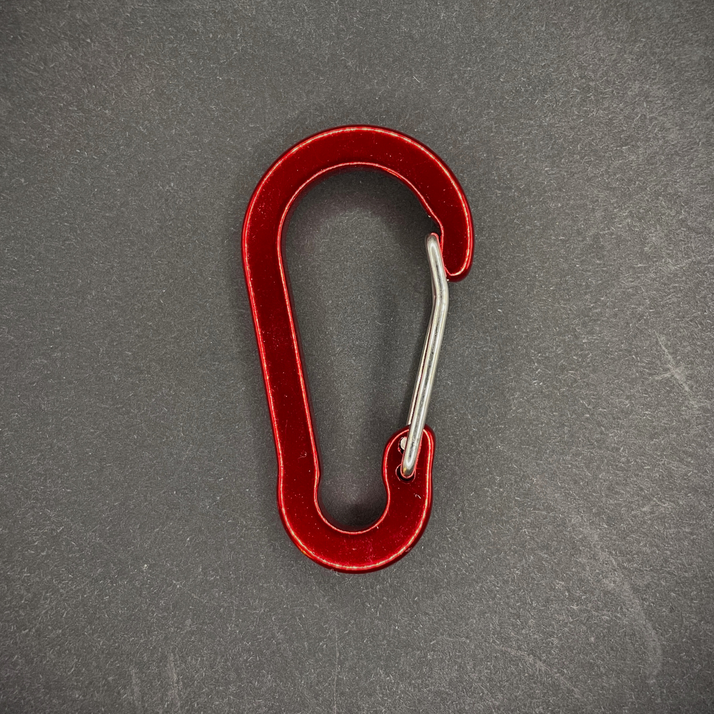 Red Anodised aluminium carabiner, arranged on a dark surface.