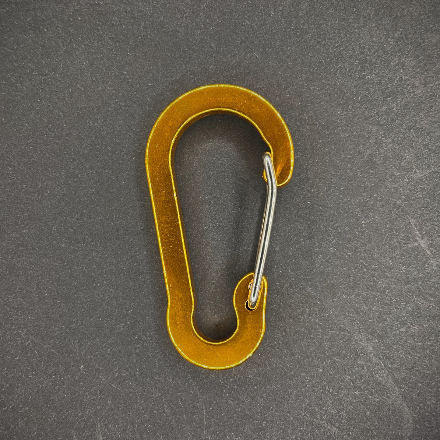 Yellow Anodised aluminium carabiner, arranged on a dark surface.