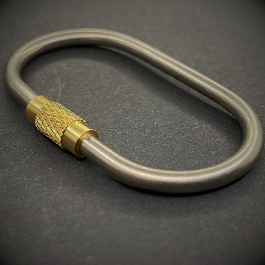 An angled view of a Mini Locking Titanium Carabiner, arranged on a dark surface