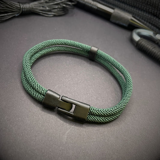 Green rope bracelet with a black metal side-release buckle and minimalist loop detail, displayed on a dark background.