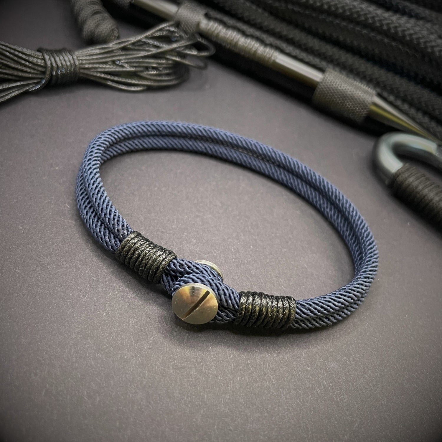Close-up of a navy rope bracelet with a screw clasp and black whipping detail, displayed on a dark surface.