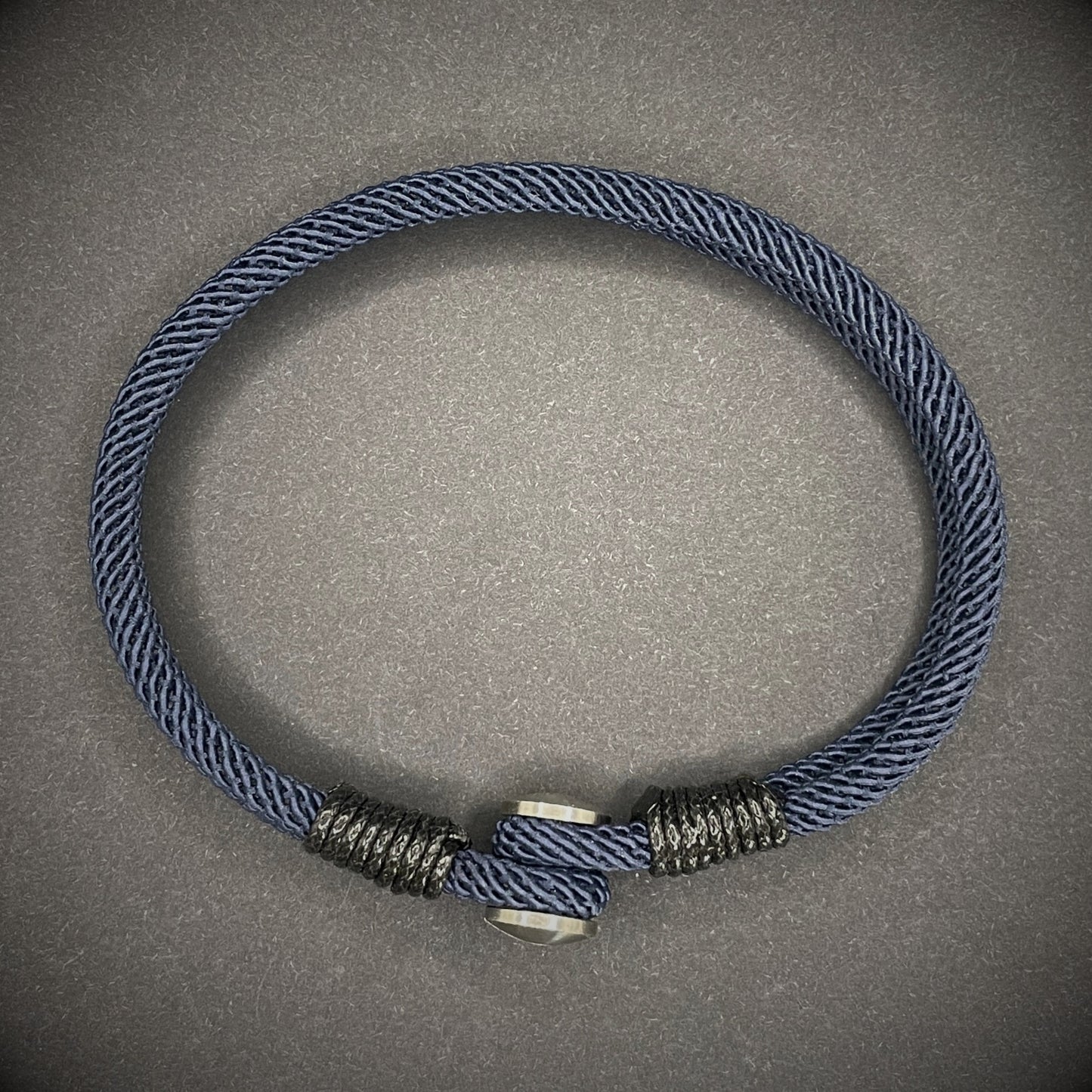 Close-up of a navy rope bracelet with a screw clasp and black whipping detail, displayed on a dark surface.