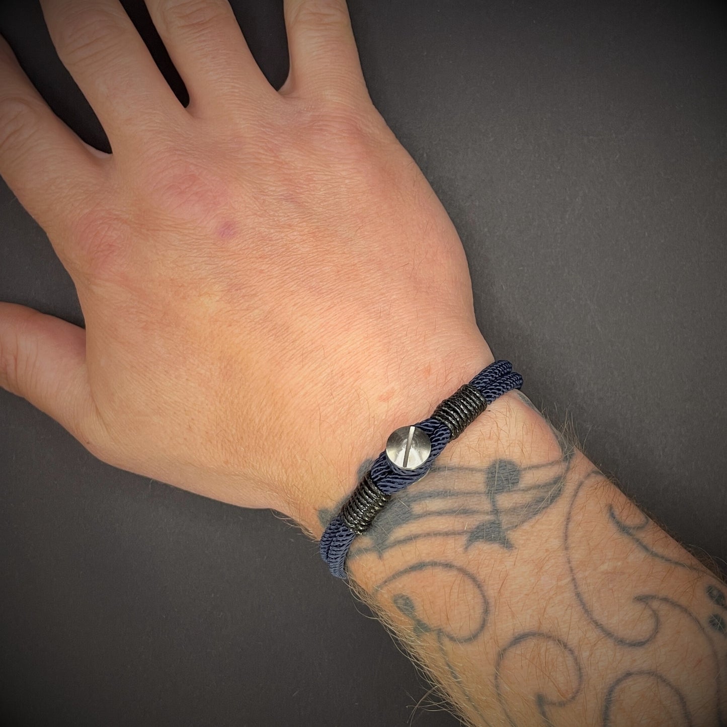 Close-up of a navy rope bracelet with a screw clasp and black whipping detail, displayed on a dark surface.