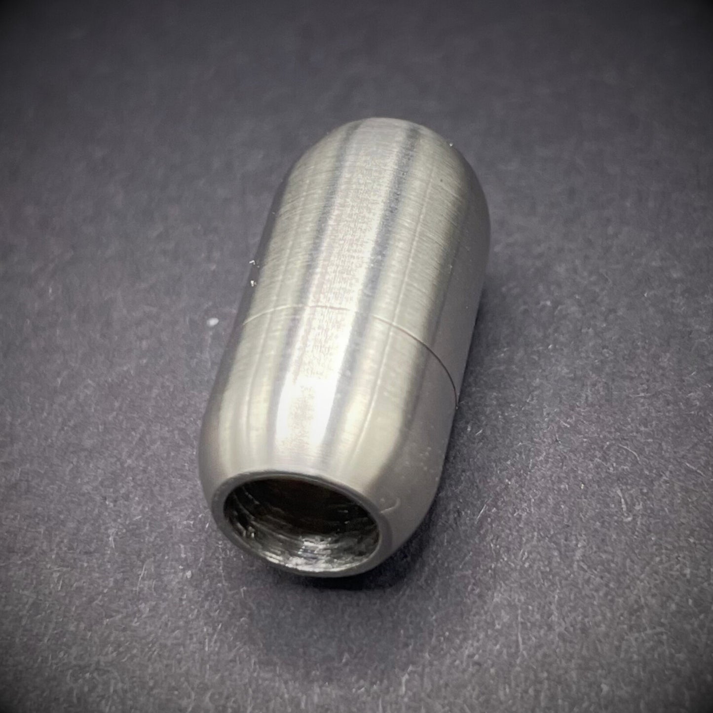 Stainless Steel cylindrical metal magnetic bracelet clasp, displayed on a dark textured background.